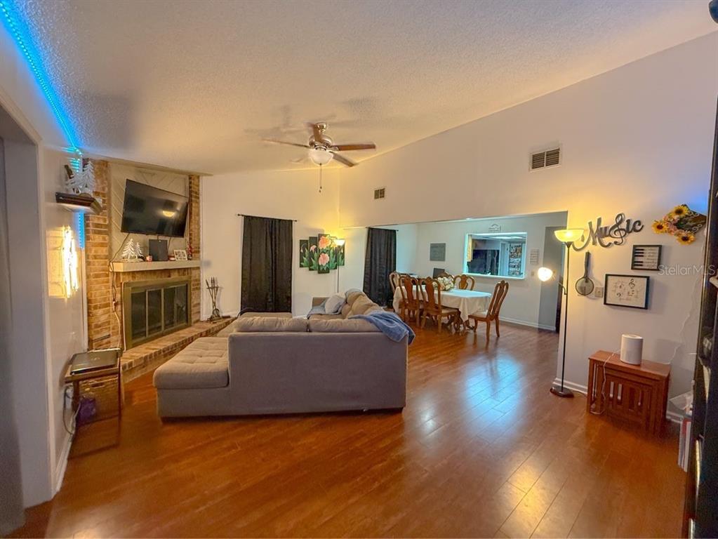 A living room with hardwood floors, a brick fireplace, and an adjacent dining area — 35058 WHISPERING OAKS BOULEVARD, DADE CITY, FL