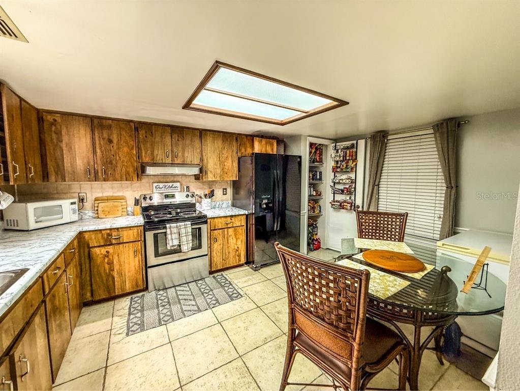 A kitchen with wood cabinets, stainless steel appliances, tile flooring, and a dining area — 35058 WHISPERING OAKS BOULEVARD, DADE CITY, FL