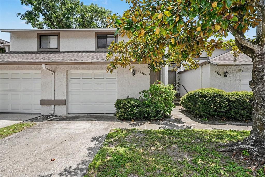 A two-story townhouse exterior features a white stucco facade, a concrete driveway, and landscaping — 12409 TITUS CT, TAMPA, FL