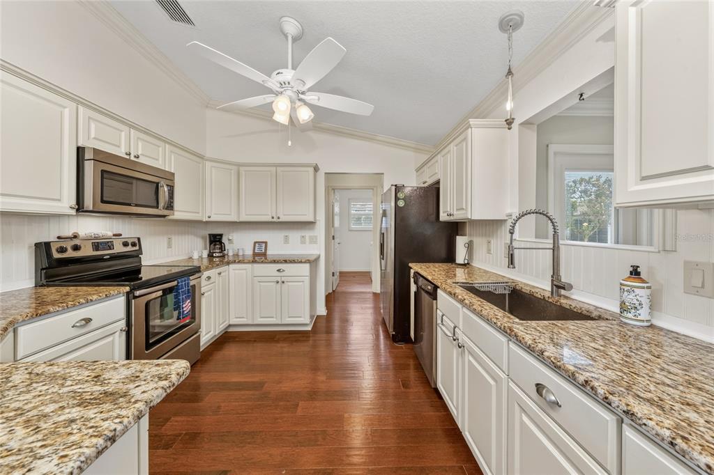 A kitchen features white cabinets, granite countertops, stainless steel appliances, and hardwood flooring — 854 FENWICK LOOP, THE VILLAGES, FL