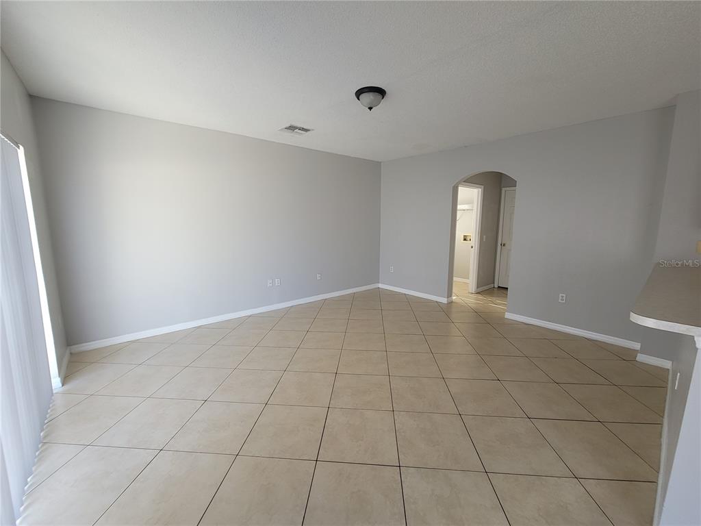 An empty room with light gray walls, beige tile flooring, and an arched doorway — 319 ALEGRIANO COURT, KISSIMMEE, FL