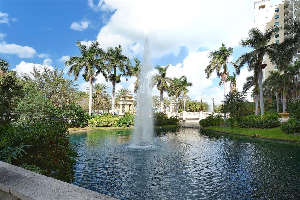 A fountain sprays water into a pond surrounded by palm trees and a stone bridge — 750 N TAMIAMI TRAIL UNIT PH08, SARASOTA, FL