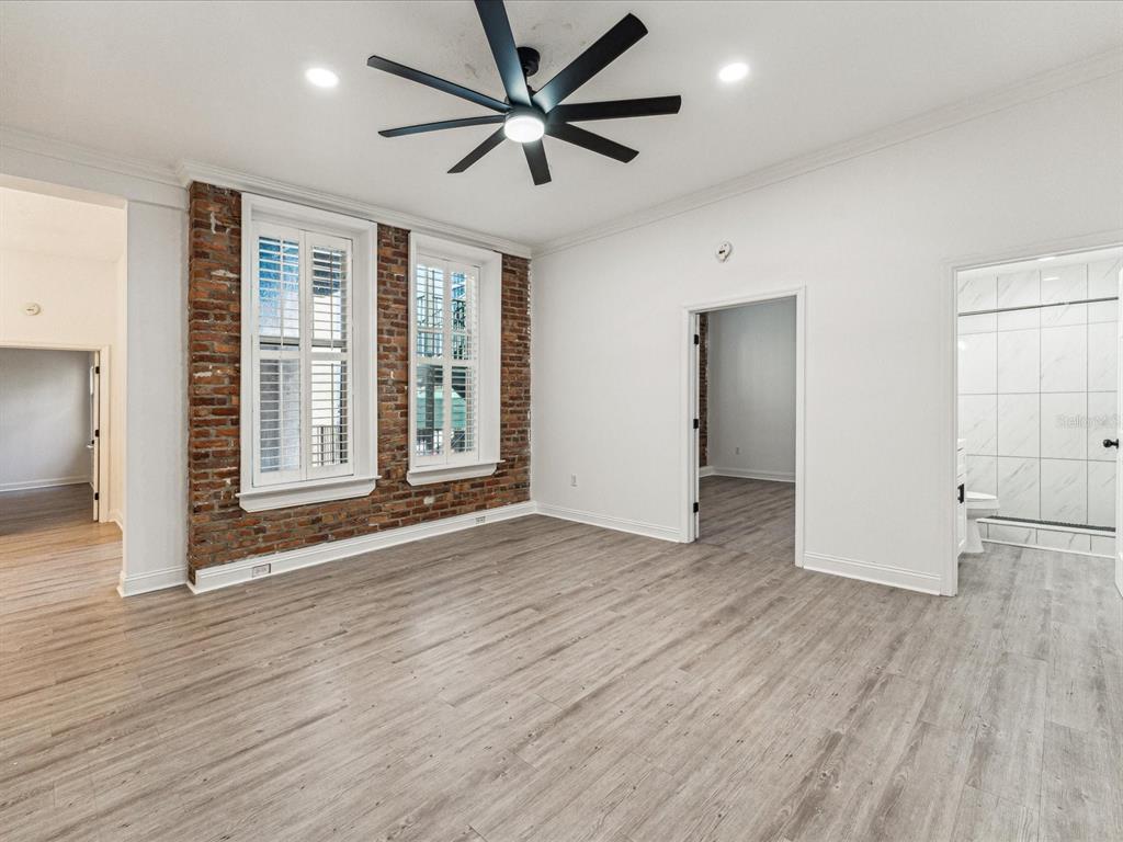A room with light wood-look flooring, white walls, a ceiling fan, and exposed brick walls — 215 CENTRAL AVENUE UNIT 3F, ST PETERSBURG, FL
