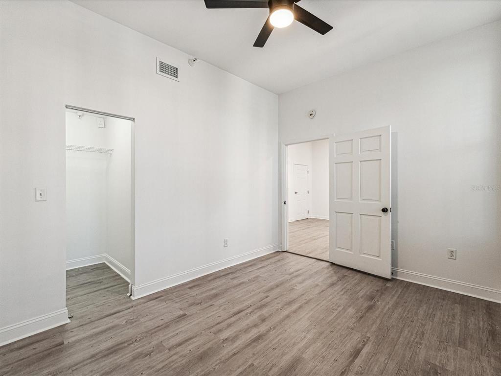An empty bedroom features light wood-look flooring, white walls, a ceiling fan, and two doorways — 215 CENTRAL AVENUE UNIT 3F, ST PETERSBURG, FL