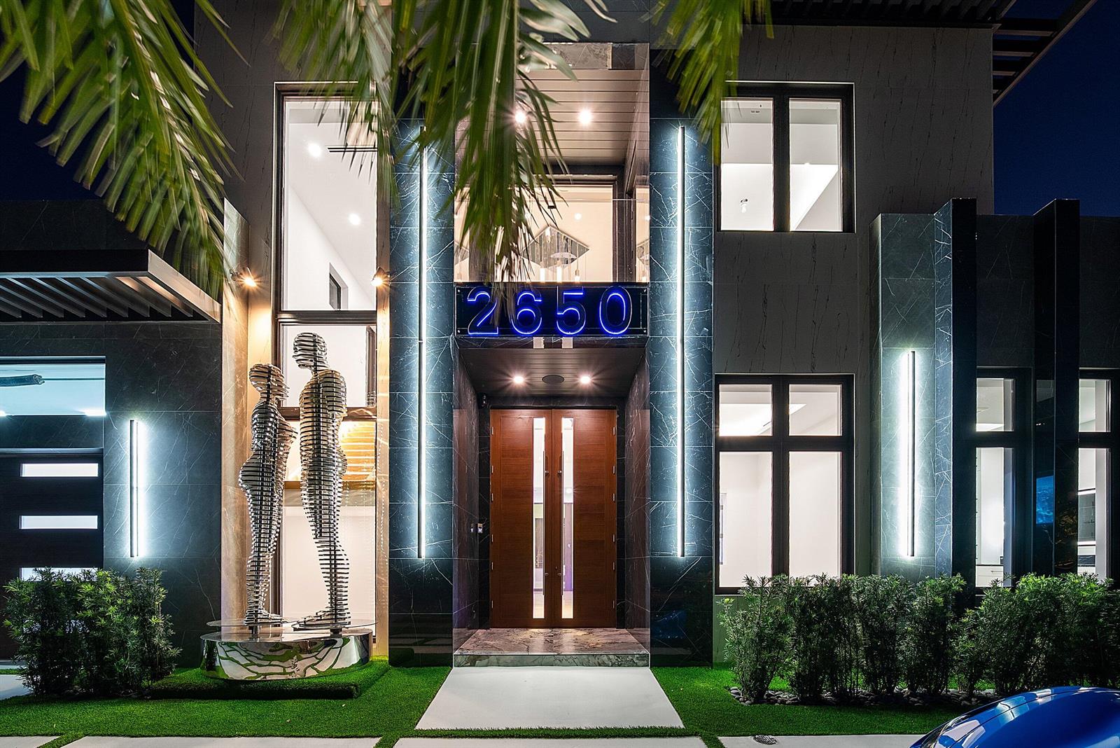 A modern two-story home exterior features dark stone cladding, vertical lighting, and metal sculpture art — 2650 NE 48th Court, Lighthouse Point FL 33064, LIGHTHOUSE POINT, FL