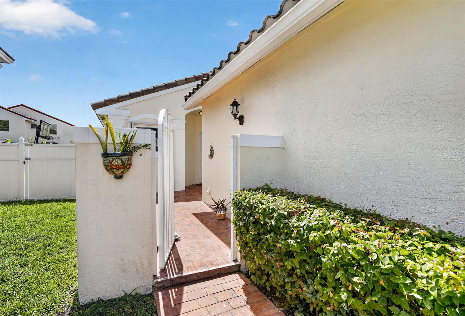 A paved walkway leads through a white gate to the entrance of a stucco home — 327 SW 191st Terrace, Pembroke Pines FL 33029, PEMBROKE PINES, FL