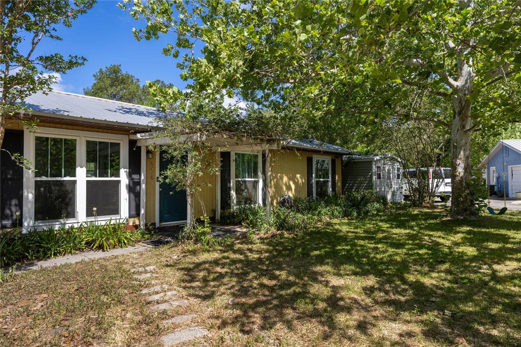 A yellow single-story house with a metal roof sits behind a large tree — 6716 NW 29TH STREET, GAINESVILLE, FL