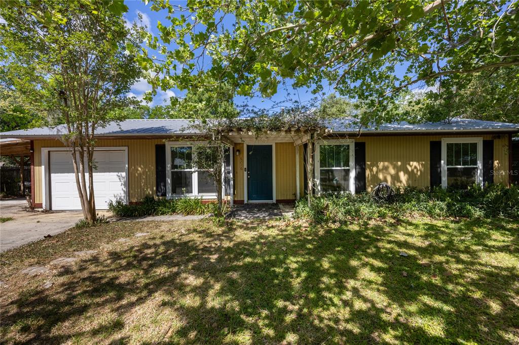 A single-story house with yellow vertical siding, a metal roof, and a front pergola — 6716 NW 29TH STREET, GAINESVILLE, FL
