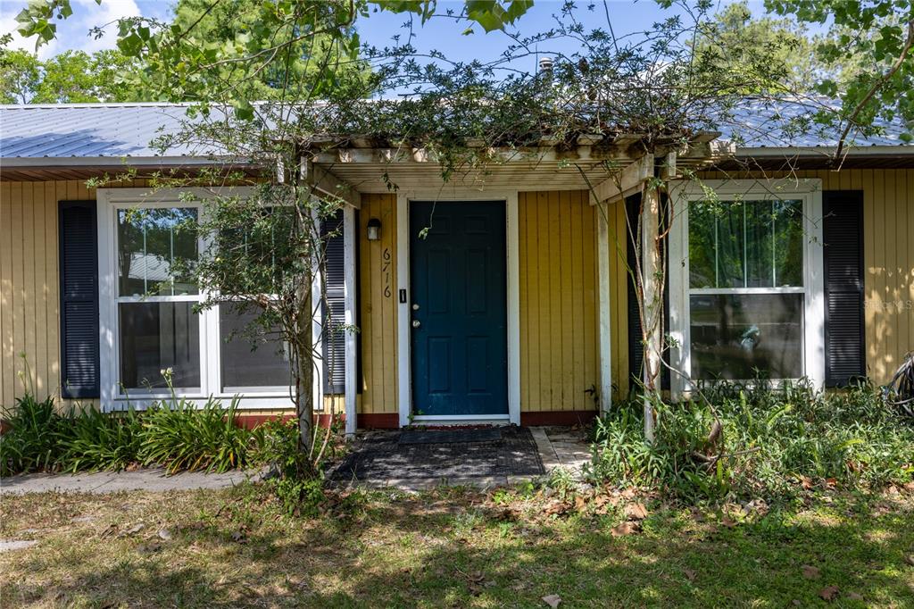 A yellow house exterior features a dark blue front door under a wooden pergola — 6716 NW 29TH STREET, GAINESVILLE, FL
