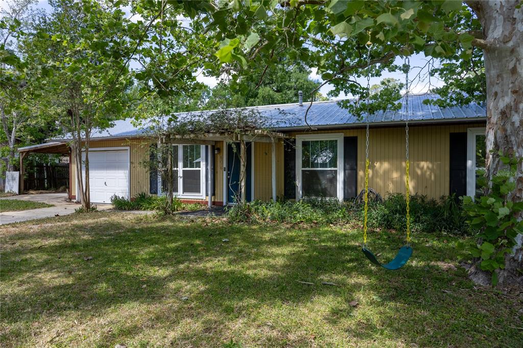 A yellow single-story house with a metal roof, attached garage, and a tree swing — 6716 NW 29TH STREET, GAINESVILLE, FL