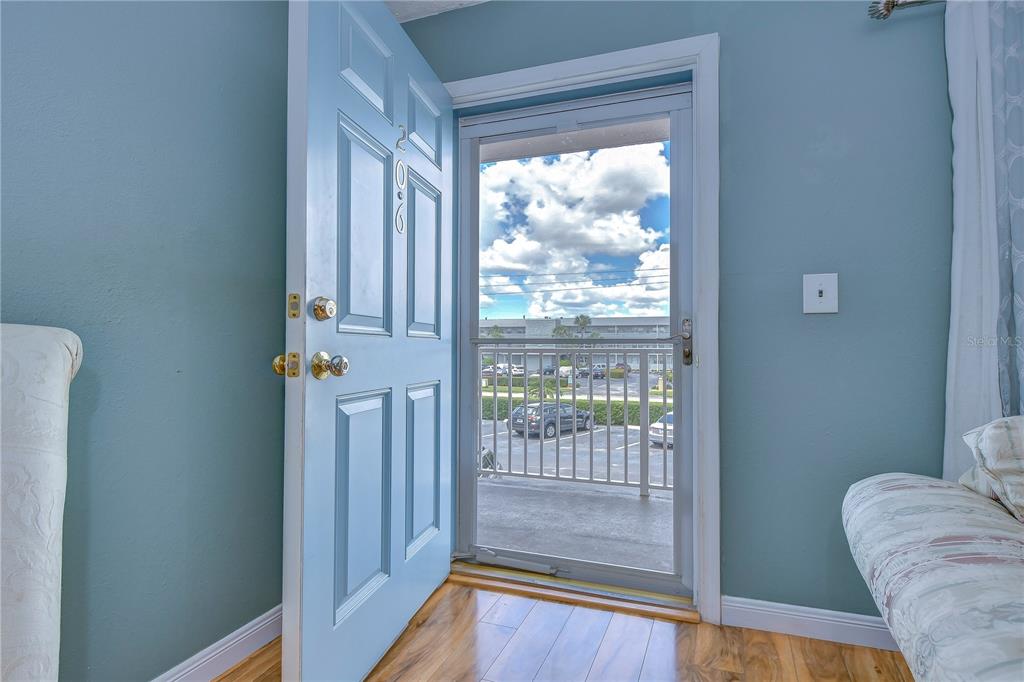 An open light blue door reveals a screen door leading to a balcony with parking — 1893 SHORE DRIVE S UNIT 206, SOUTH PASADENA, FL