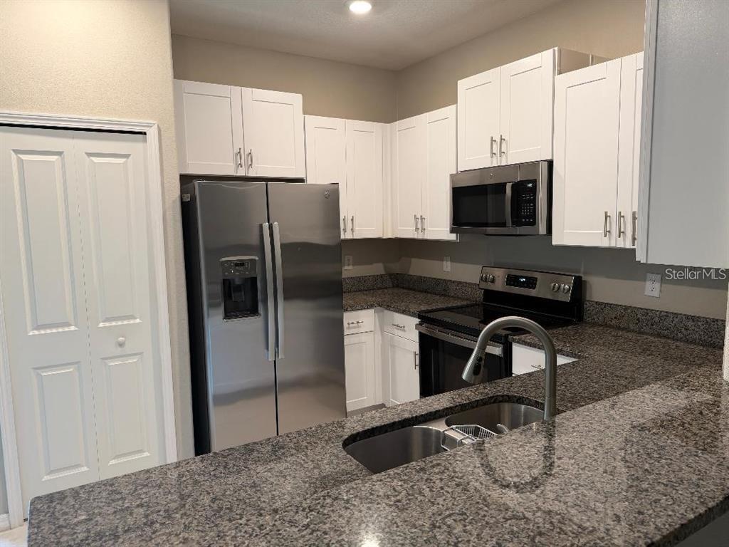 A kitchen features white cabinets, stainless steel appliances, and dark granite countertops — 11905 CASTINE STREET, NEW PORT RICHEY, FL