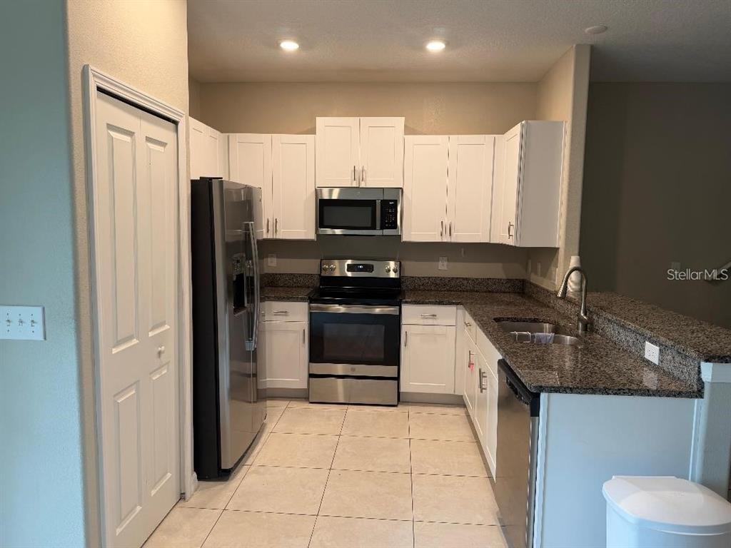 A kitchen features white cabinets, stainless steel appliances, and dark granite countertops — 11905 CASTINE STREET, NEW PORT RICHEY, FL