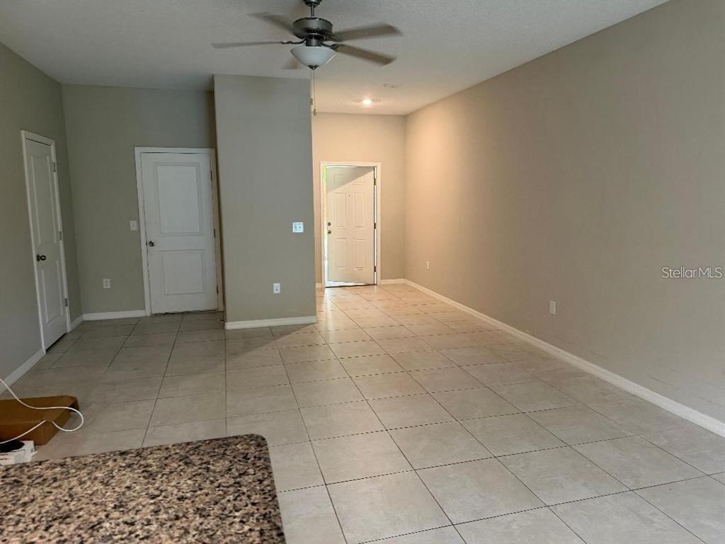 An interior view shows a room with light-colored tile flooring, beige walls, and a ceiling fan — 11905 CASTINE STREET, NEW PORT RICHEY, FL