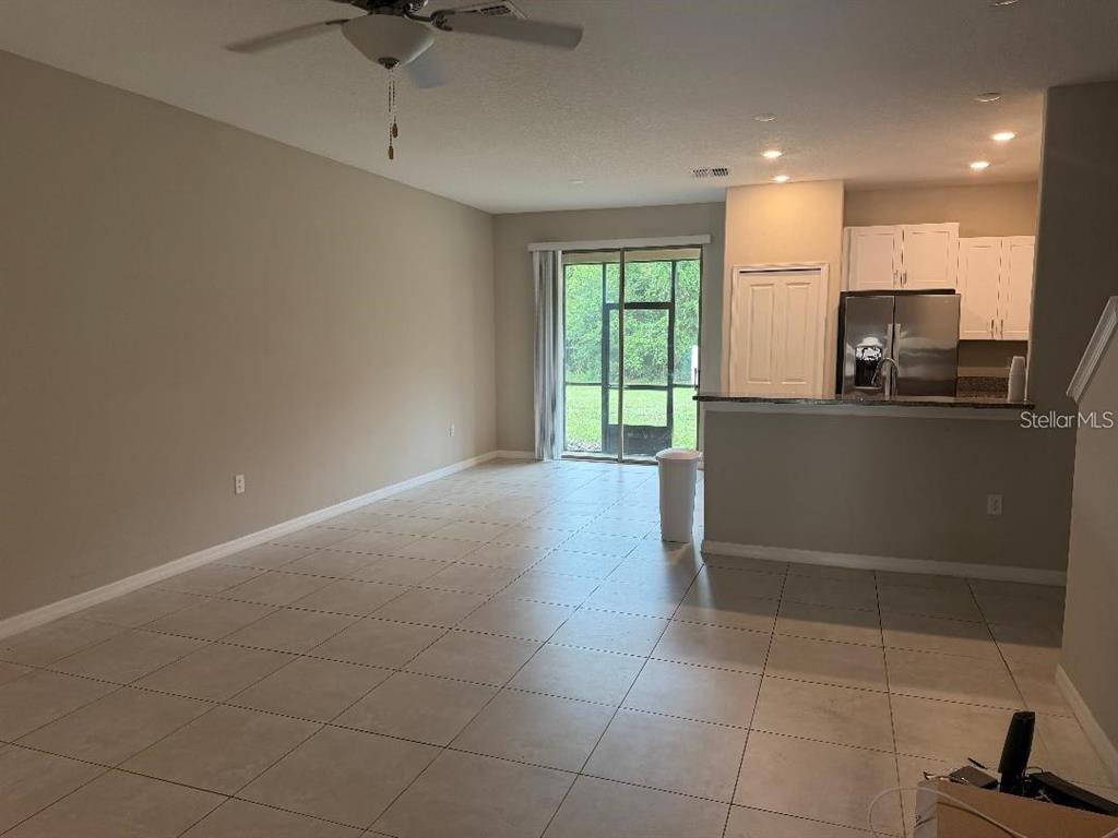 An open-concept living area features light-colored tile flooring, a ceiling fan, and a kitchen — 11905 CASTINE STREET, NEW PORT RICHEY, FL