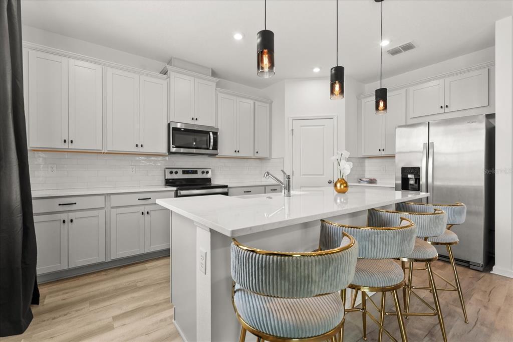 A modern kitchen features white cabinets, a quartz island with bar stools, and stainless appliances — 9098 BEACH TEA WAY, KISSIMMEE, FL