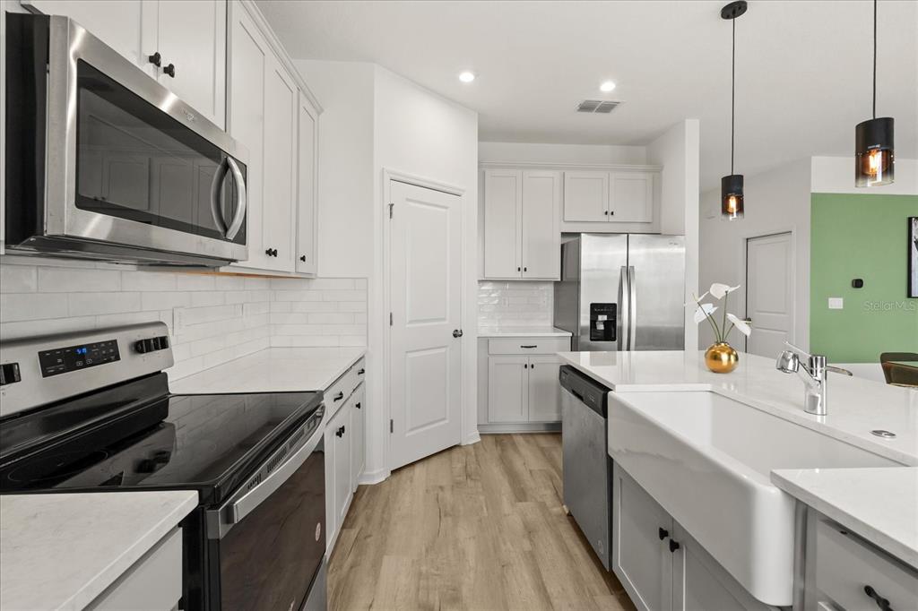 A modern kitchen features white cabinetry, stainless steel appliances, a farmhouse sink, and light flooring — 9098 BEACH TEA WAY, KISSIMMEE, FL
