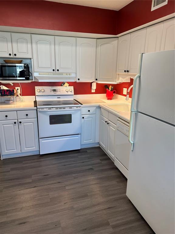 A kitchen features white cabinets, a white stove, a white refrigerator, and dark wood flooring — 2448 COLUMBIA DRIVE UNIT 28, CLEARWATER, FL