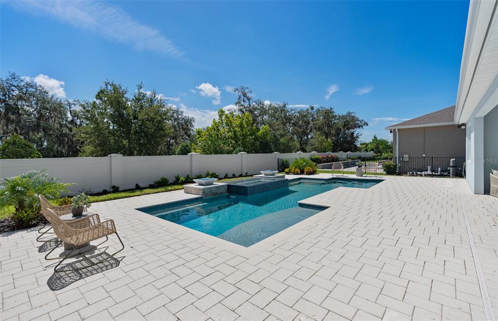 A backyard features a rectangular swimming pool with a spa, stone pavers, and a white fence — 6213 CITRUS GROVE COURT, ST CLOUD, FL