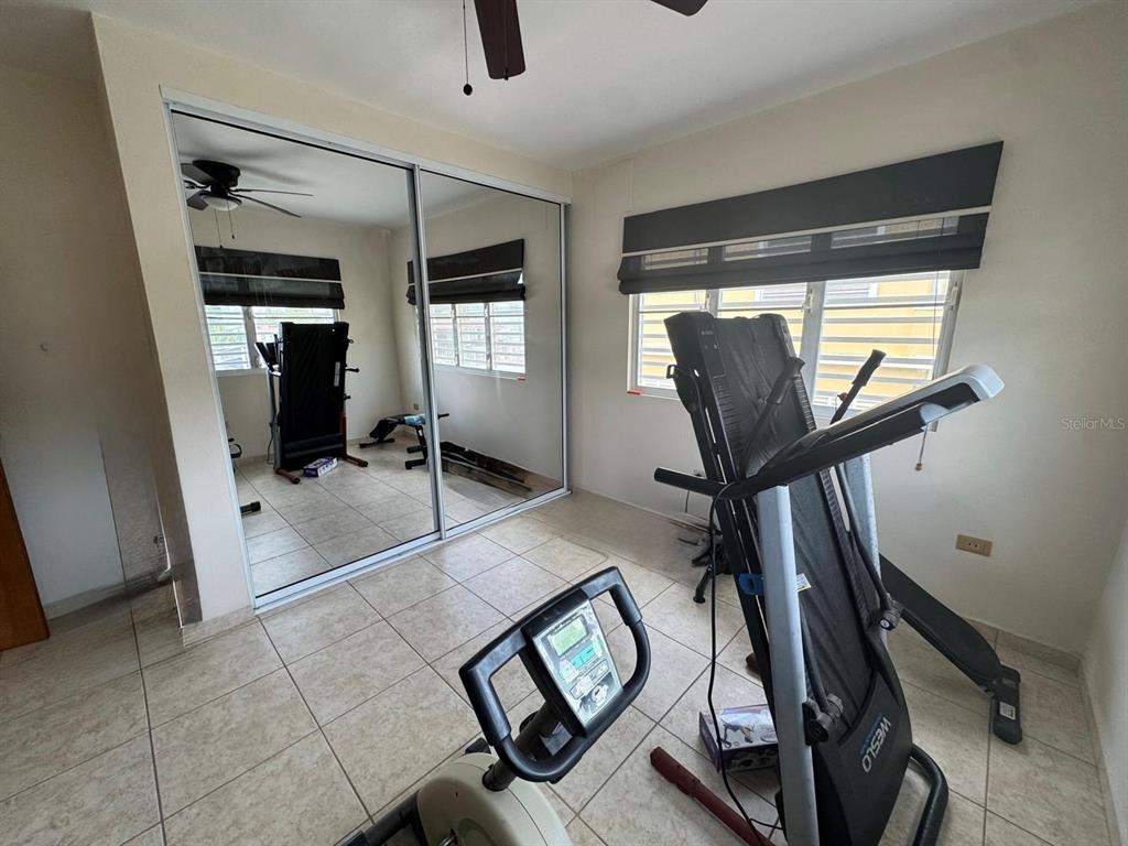 A home gym room features tile flooring, mirrored closet doors, and a window with blinds — 2 B-15 URB. ALTURAS DE MONTE BRISAS, GURABO, PR