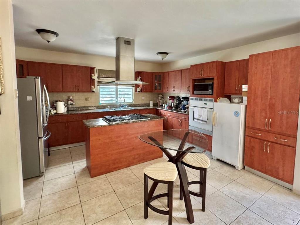 A kitchen features wood cabinets, a center island with a cooktop, and tile flooring — 2 B-15 URB. ALTURAS DE MONTE BRISAS, GURABO, PR