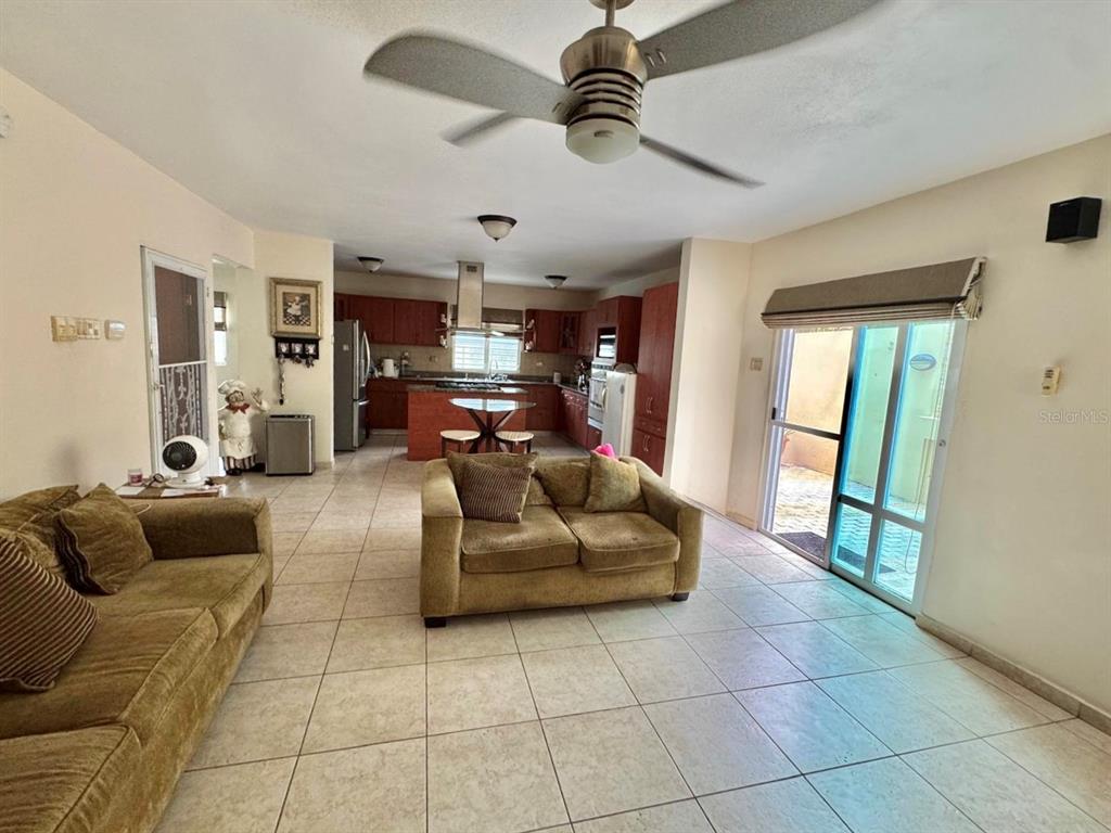 An open-concept living room with tile flooring leads into a kitchen with wooden cabinetry — 2 B-15 URB. ALTURAS DE MONTE BRISAS, GURABO, PR