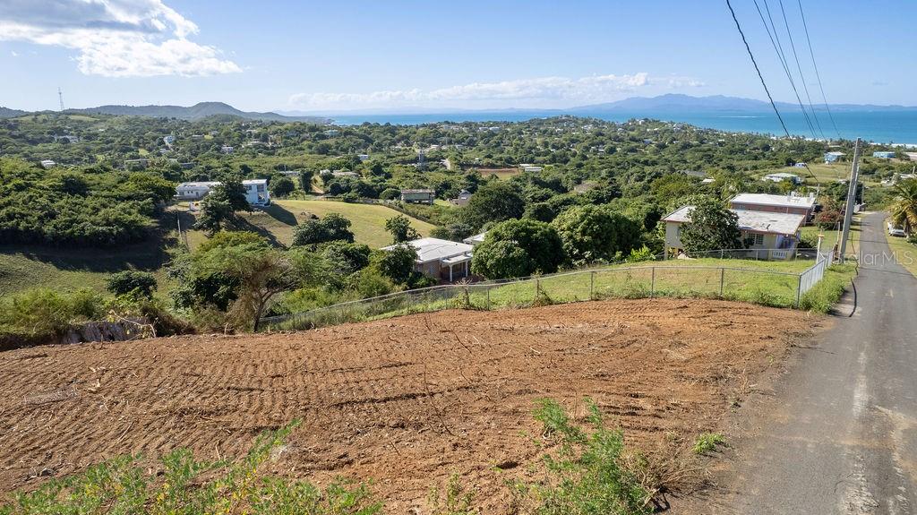 A vacant, sloped dirt lot overlooks a coastal landscape with houses and the ocean — 583 CALLE 16, VIEQUES, PR