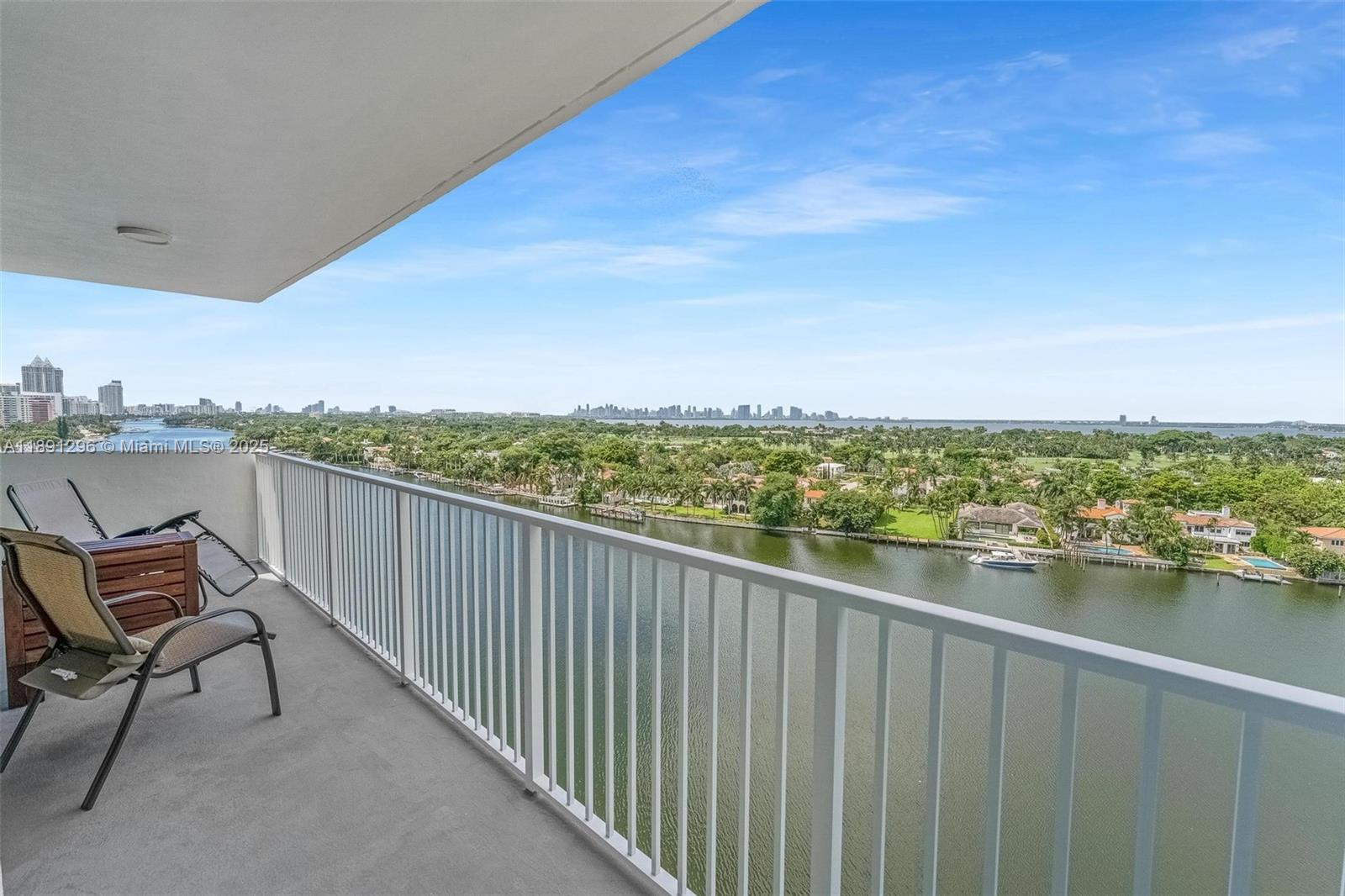 A balcony with metal railings overlooks a waterway, a golf course, and a distant city skyline — 5838 Collins Ave # 11B, Miami Beach FL 33140, MIAMI BEACH, FL