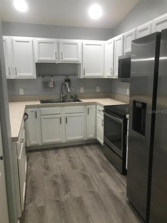 A kitchen features white cabinets, stainless steel appliances, light countertops, and wood-look flooring — 12377 NE 50TH VIEW, OXFORD, FL