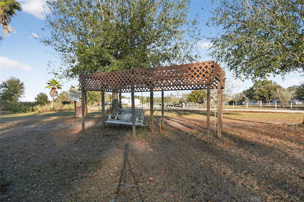 A wooden lattice-covered pergola stands over a white porch swing in a grassy yard — 2774 SNIPE DRIVE, ZOLFO SPRINGS, FL
