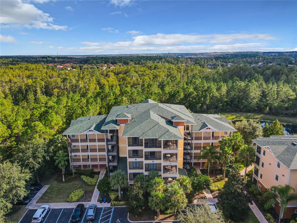An aerial view of a multi-story apartment building surrounded by trees and a parking lot — 9061 TREASURE TROVE LANE UNIT 403, KISSIMMEE, FL