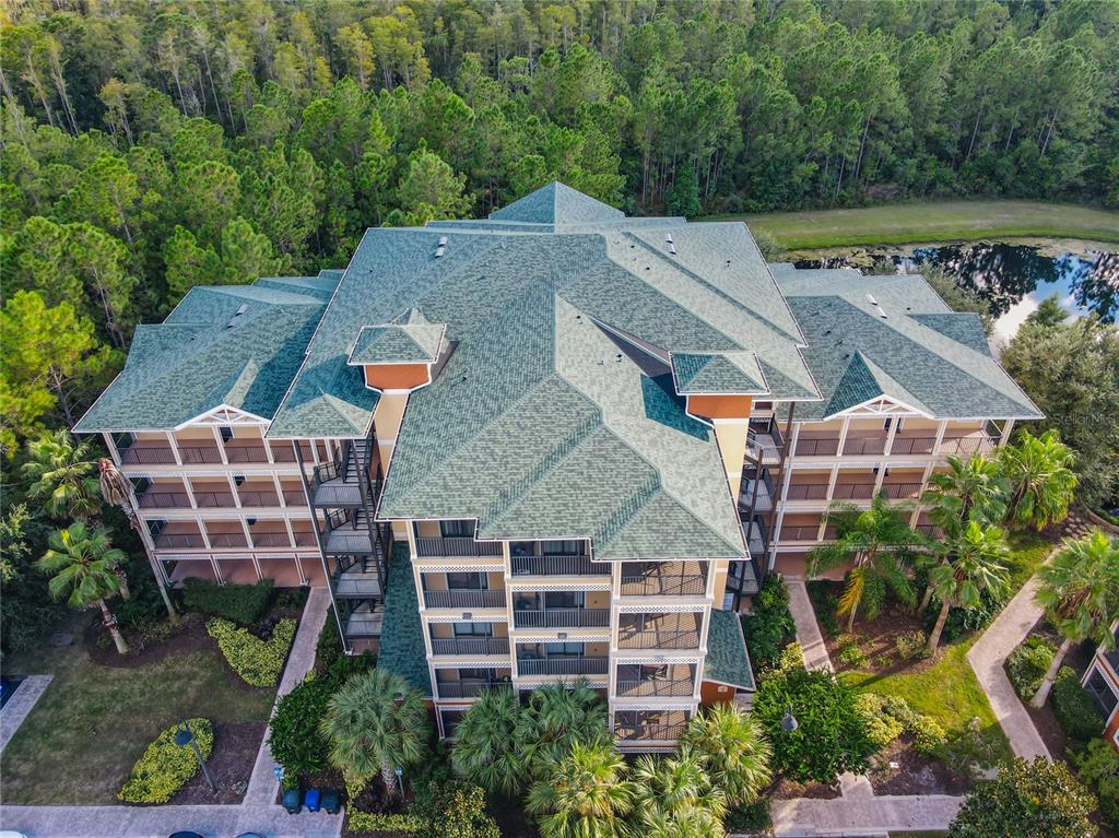 An aerial view shows a multi-story apartment building with a green roof surrounded by trees — 9061 TREASURE TROVE LANE UNIT 403, KISSIMMEE, FL