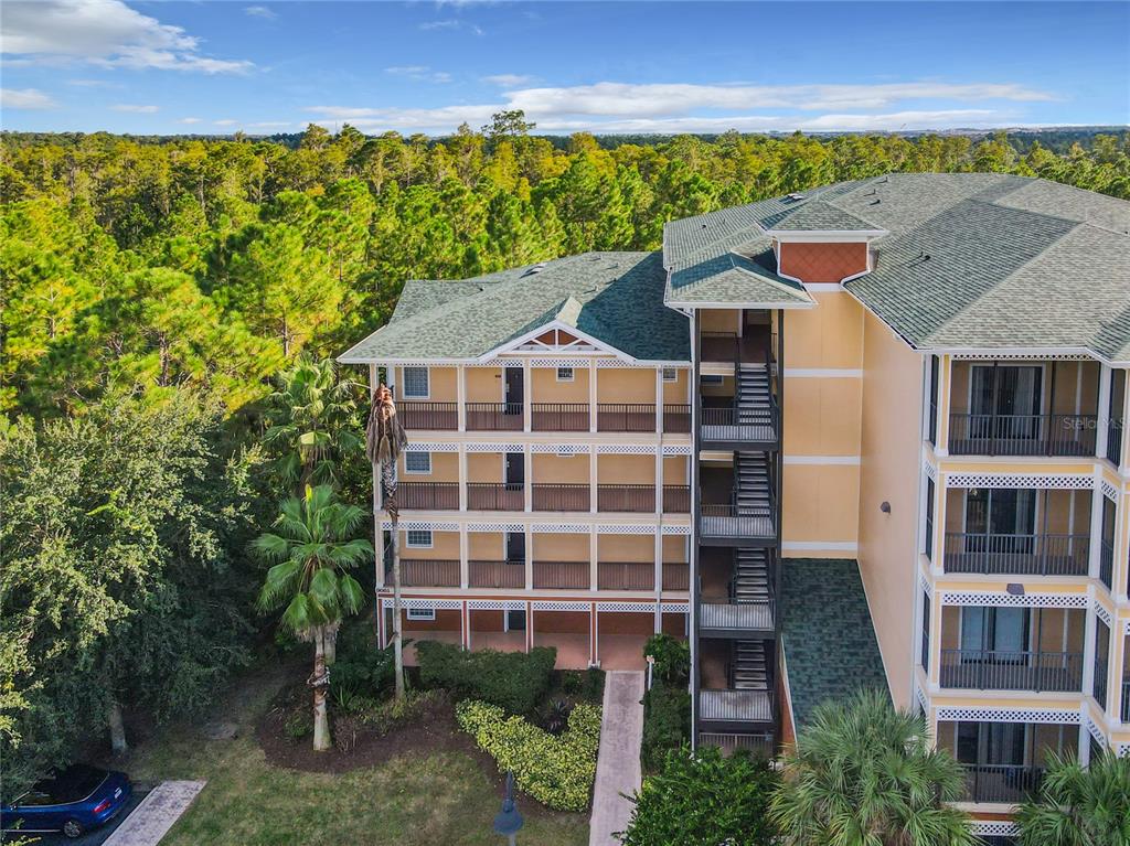 An exterior view of a multi-story apartment building with balconies and an adjacent forest — 9061 TREASURE TROVE LANE UNIT 403, KISSIMMEE, FL