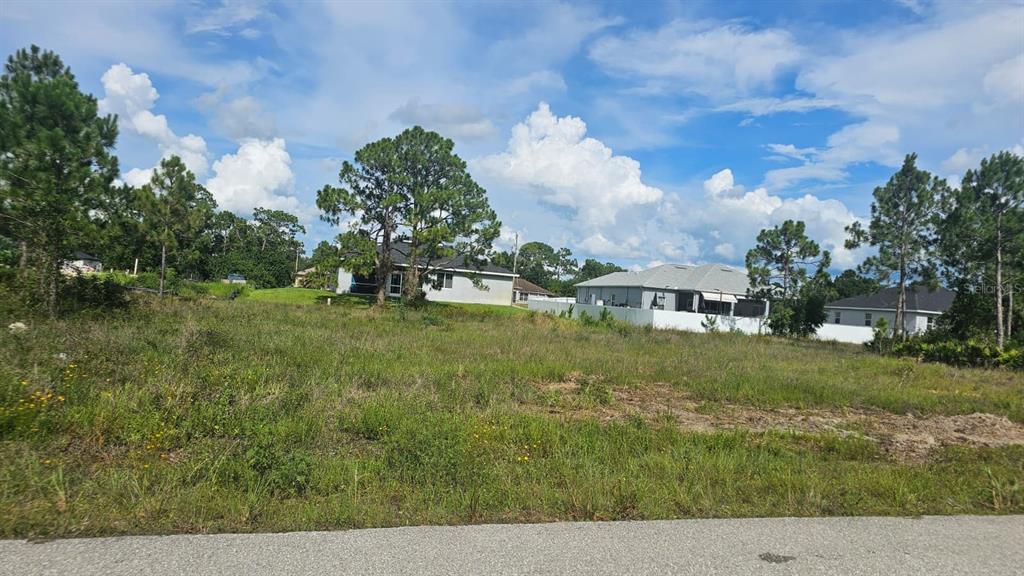 A vacant, grassy residential lot sits in front of several suburban houses under a cloudy sky — 1400 VENICE AVENUE N, LEHIGH ACRES, FL