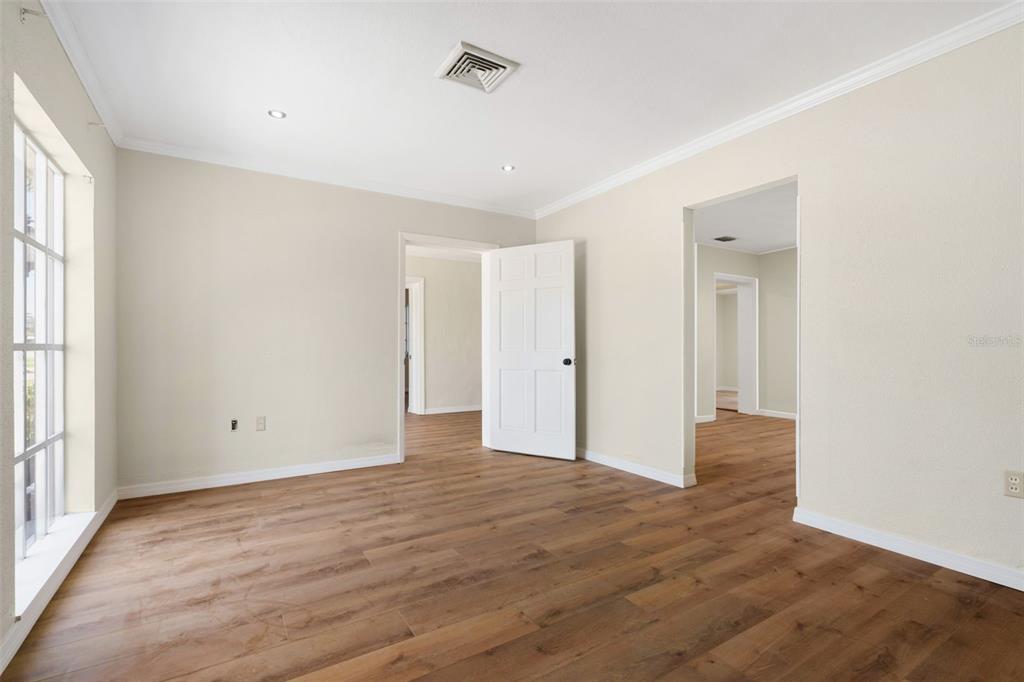 An empty room features light-colored walls, wood-look flooring, a white door, and two doorways — 1455 COURT STREET, CLEARWATER, FL