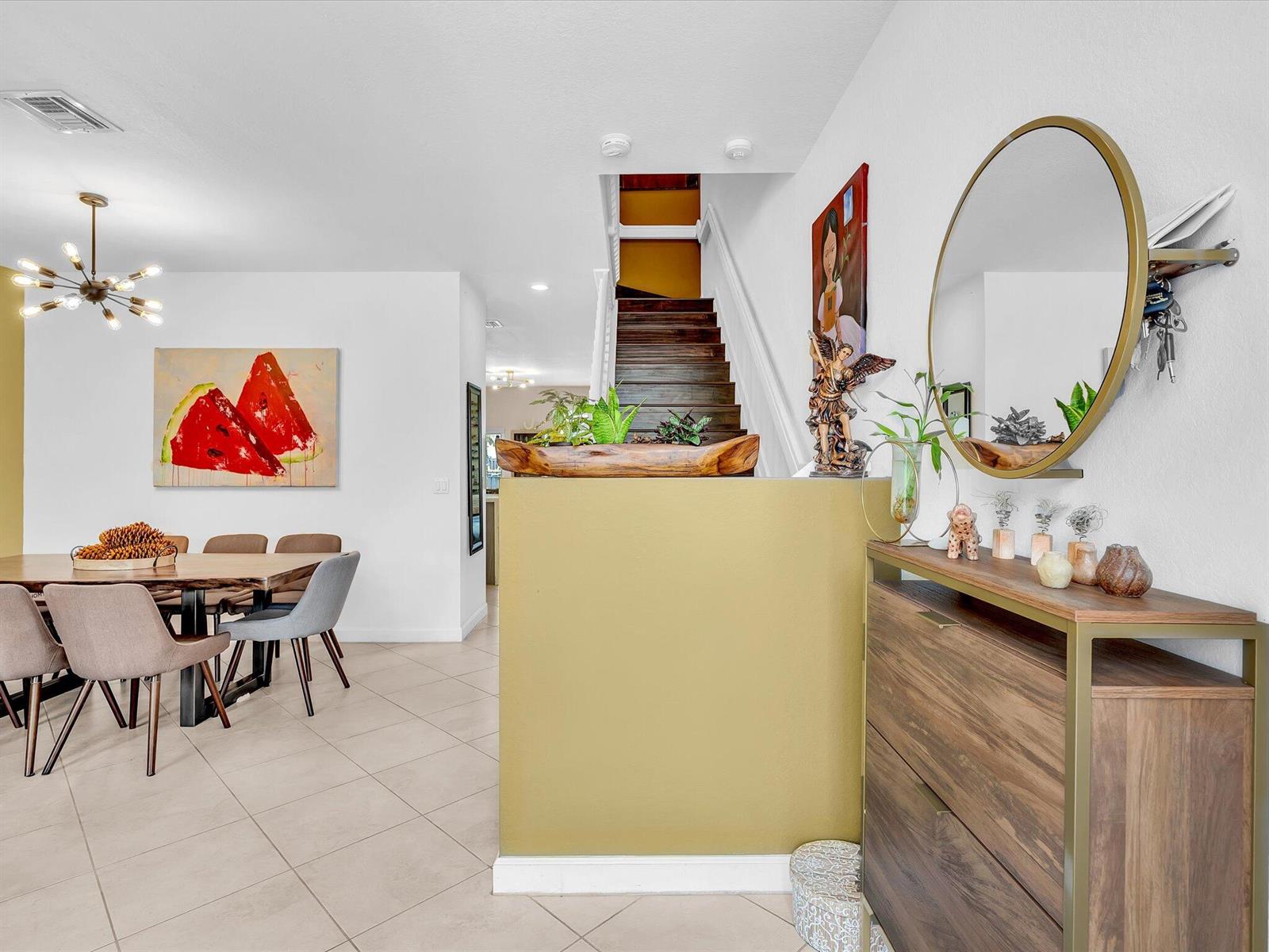 A dining area with a watermelon painting and a staircase behind a mustard-colored half wall — 5331 Ashley River Road, West Palm Beach FL 33417, WEST PALM BEACH, FL