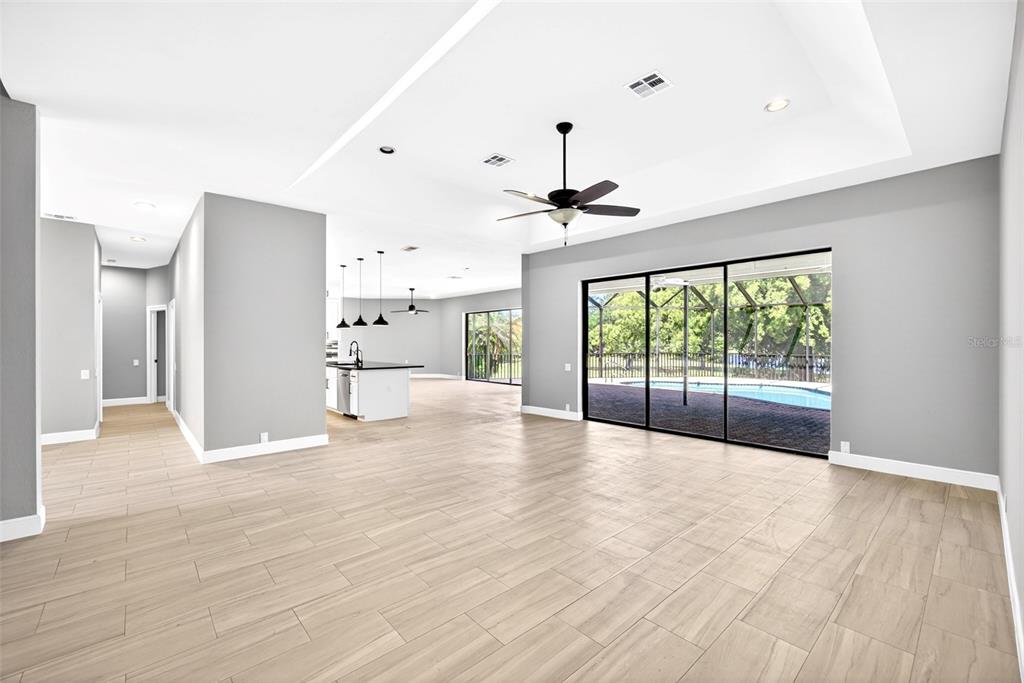 A spacious living area with light wood-look tile floors, a tray ceiling, and sliding glass doors — 7214 HENDRY CREEK DRIVE, FORT MYERS, FL