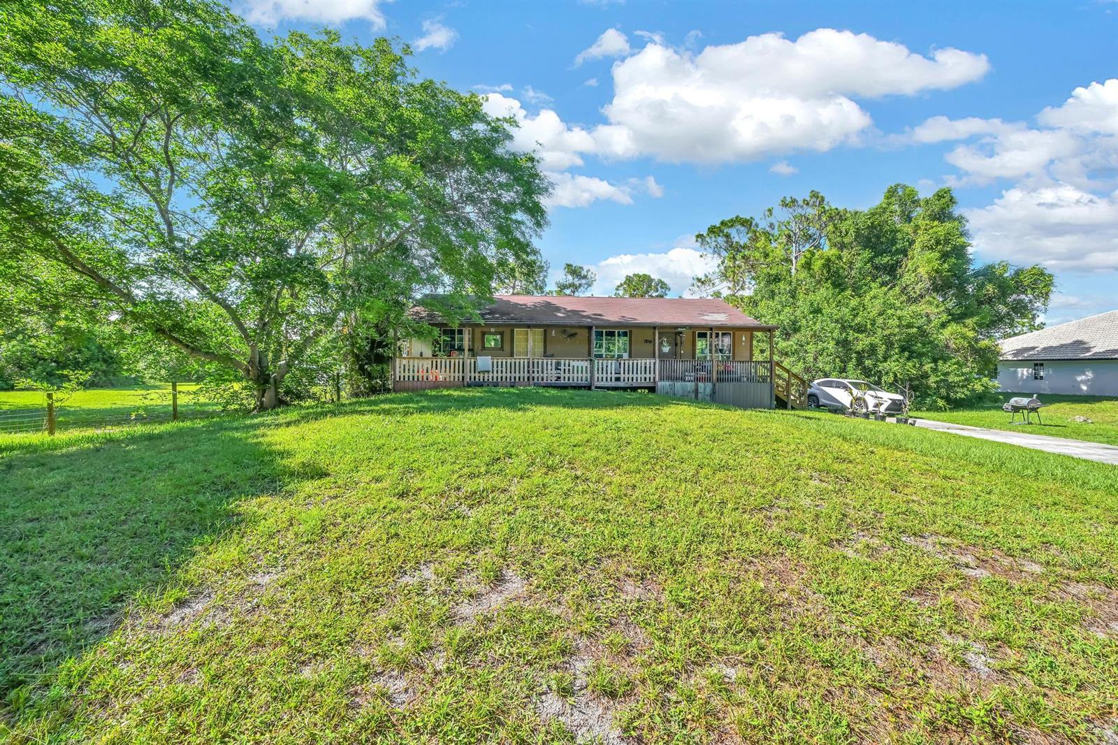 A single-story house with a wooden porch sits behind a large, grassy front yard — 17605 92nd Lane N, FL 33470, FL