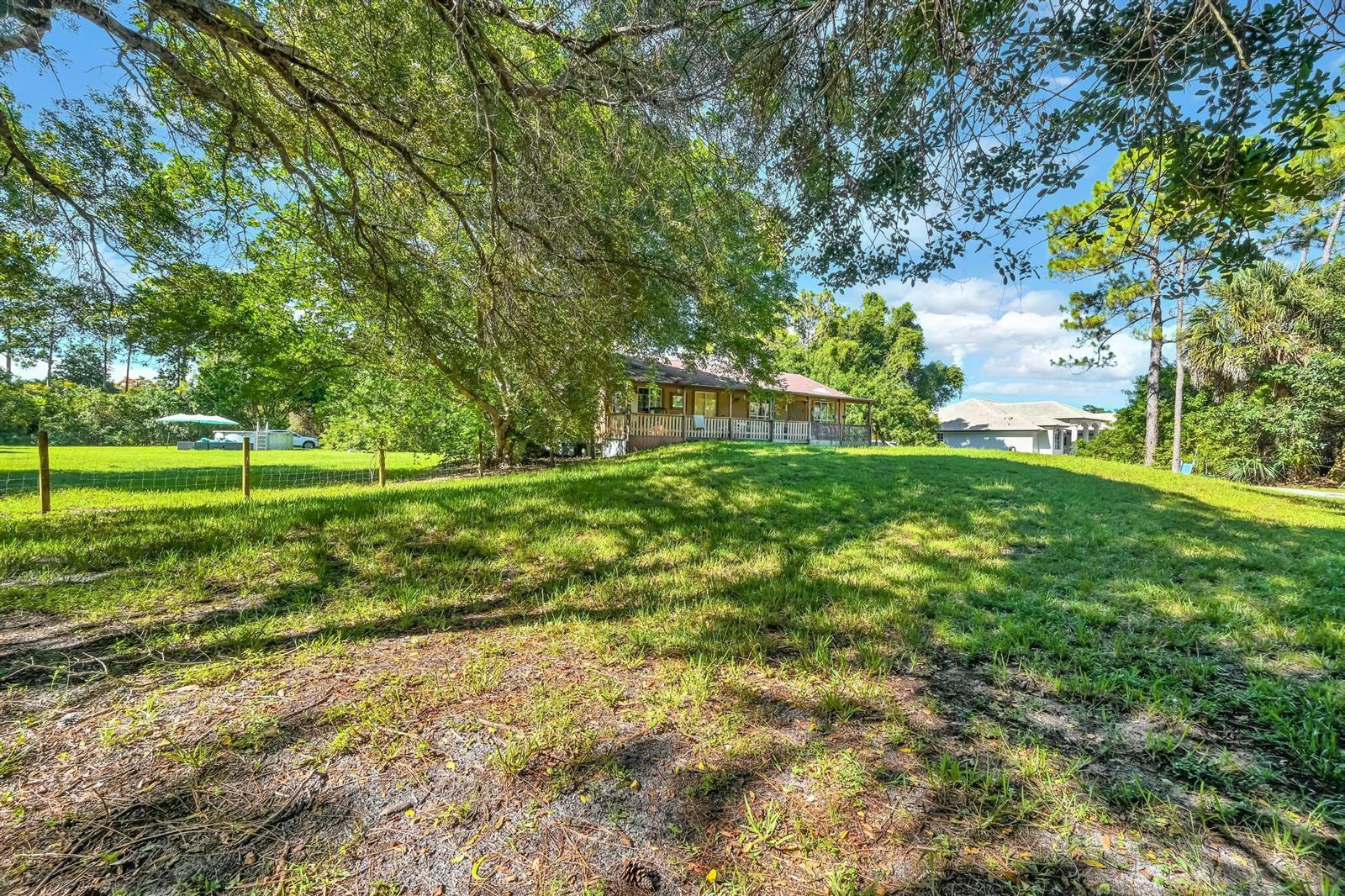 A house with a wooden porch sits behind a large grassy yard under mature trees — 17605 92nd Lane N, FL 33470, FL