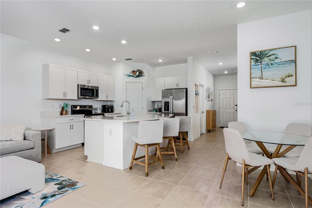 A bright, open-concept kitchen features white cabinetry, a center island with barstools, and dining area — 6011 WHETSTONE COURT, PALMETTO, FL