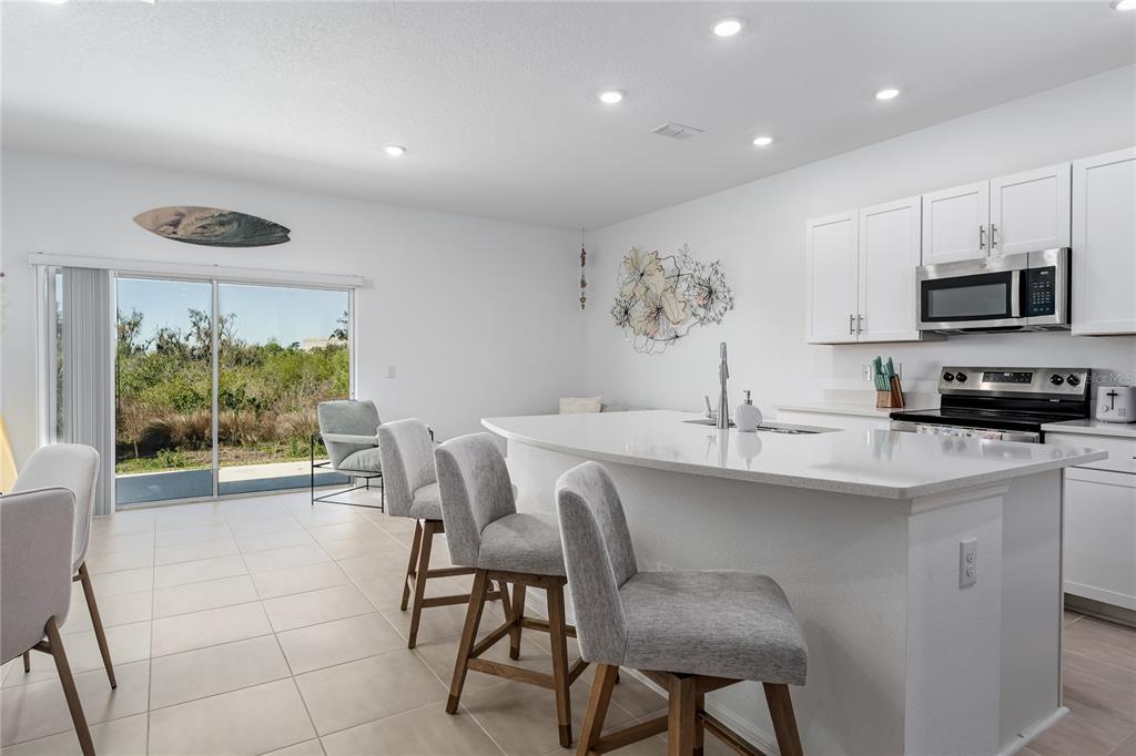 A modern kitchen features white cabinetry, a quartz island with bar seating, and tile flooring — 6011 WHETSTONE COURT, PALMETTO, FL