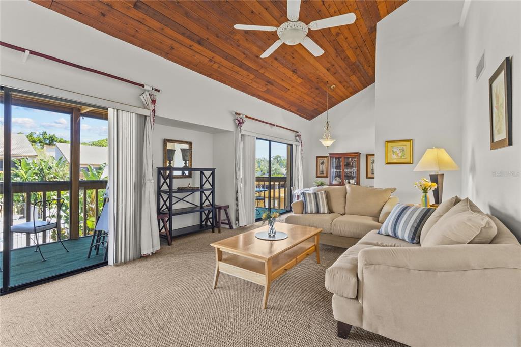 A living room features a wood-paneled vaulted ceiling, beige sofas, and sliding glass balcony doors — 3033 WILLOW GREEN UNIT 10, SARASOTA, FL