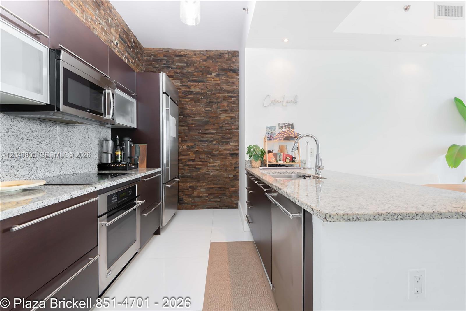 A modern kitchen features dark cabinetry, granite countertops, and a stacked stone accent wall — 950 Brickell Bay Dr # 4701, Miami FL 33131, MIAMI, FL