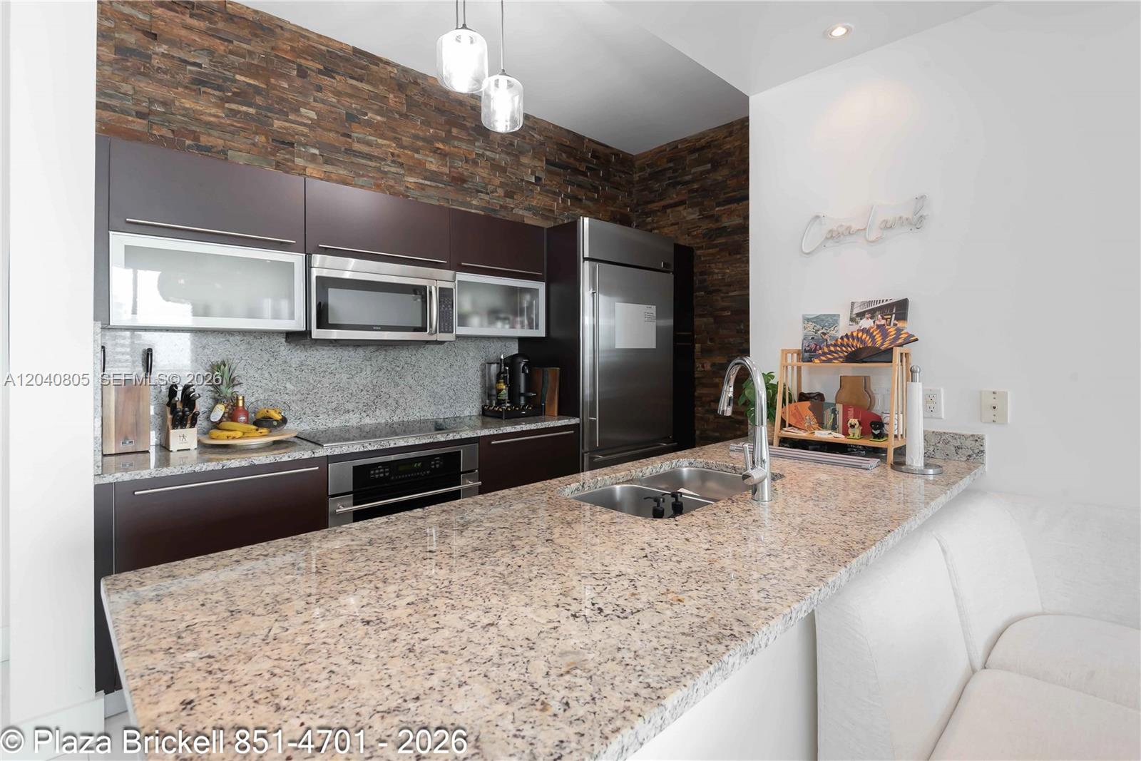 A kitchen features dark brown cabinetry, granite countertops, and a stacked stone accent wall — 950 Brickell Bay Dr # 4701, Miami FL 33131, MIAMI, FL
