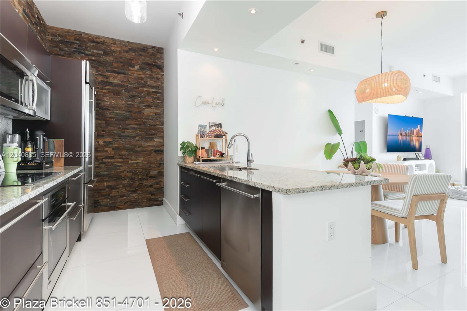 A modern kitchen features dark cabinetry, a stone accent wall, and a granite-topped island — 950 Brickell Bay Dr # 4701, Miami FL 33131, MIAMI, FL