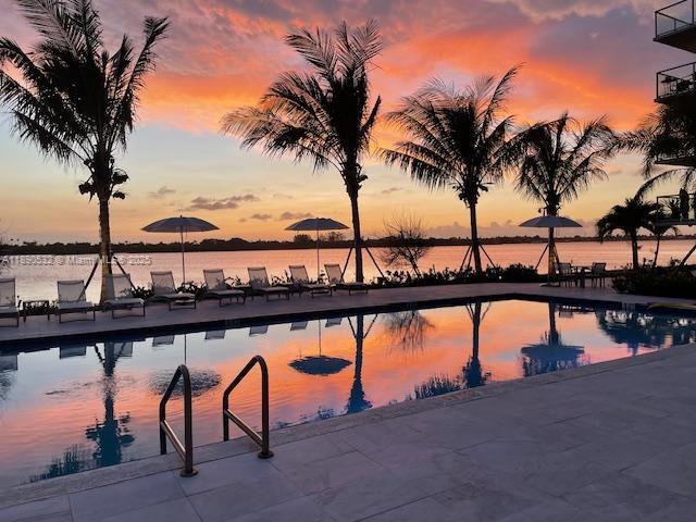 A swimming pool overlooks a lake at sunset with palm trees and lounge chairs nearby — 2560 S Ocean Blvd # 312, Palm Beach FL 33480, PALM BEACH, FL