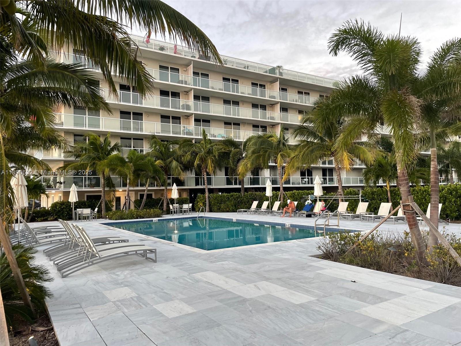 A multi-story apartment building overlooks a swimming pool surrounded by lounge chairs and palm trees — 2560 S Ocean Blvd # 312, Palm Beach FL 33480, PALM BEACH, FL
