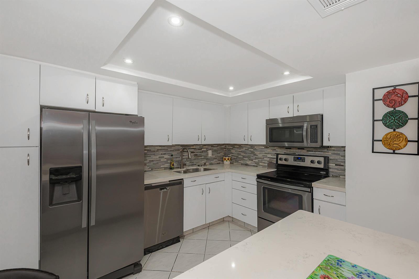A kitchen with white cabinets, stainless steel appliances, a tiled backsplash, and a central island — 1333 E Hallandale Beach Boulevard # 101, Hallandale Beach FL 33009, HALLANDALE BEACH, FL