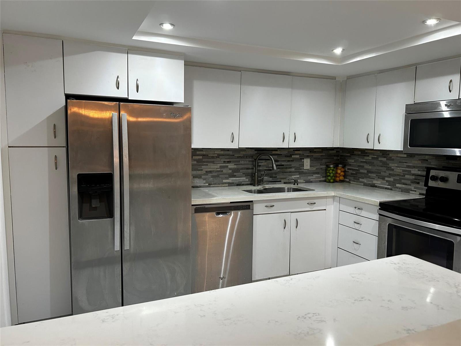 A kitchen features white cabinets, stainless steel appliances, a stone backsplash, and white countertops — 1333 E Hallandale Beach Boulevard # 101, Hallandale Beach FL 33009, HALLANDALE BEACH, FL