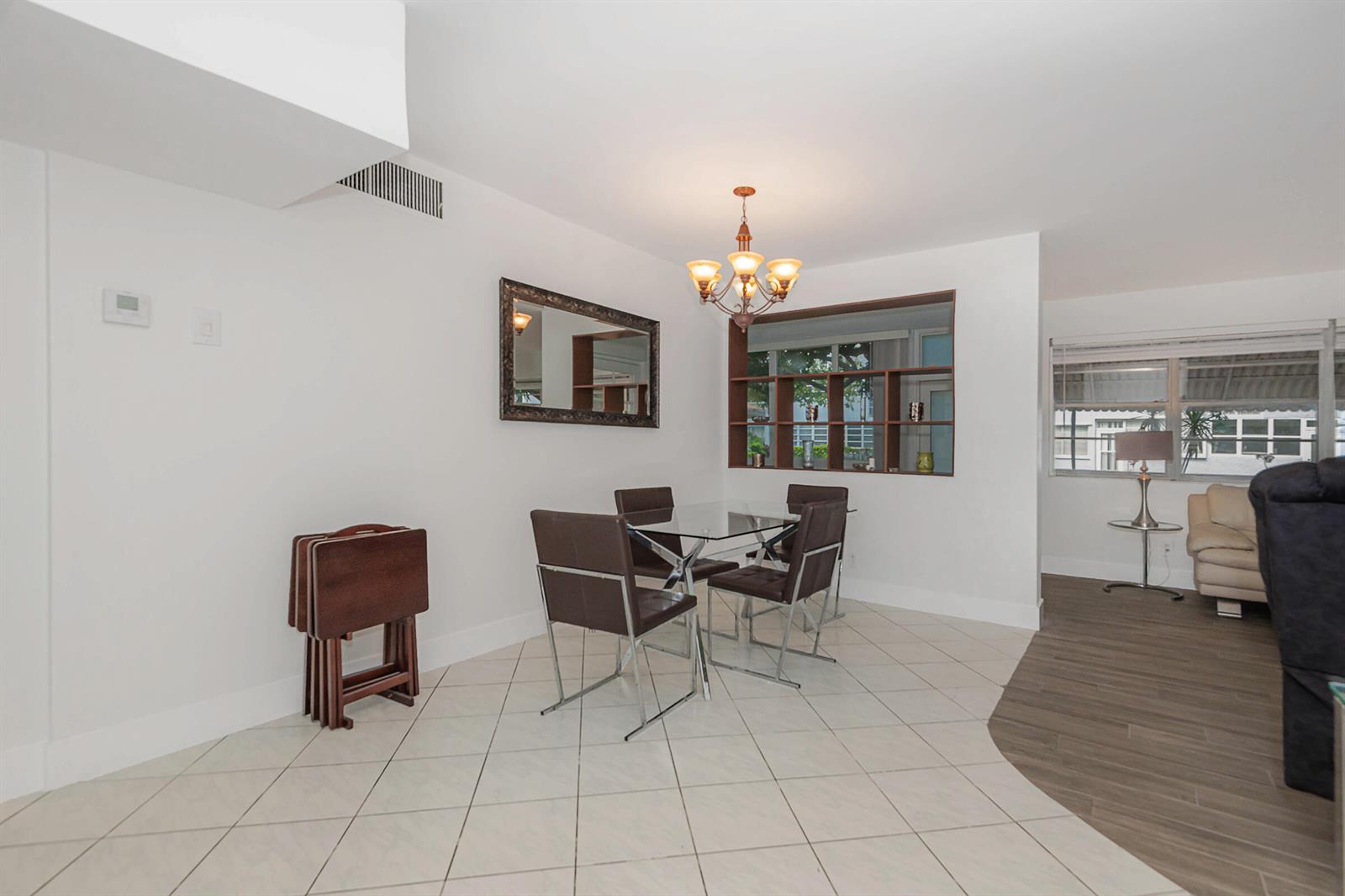 A dining area features a glass table, four brown chairs, a chandelier, and tiled flooring — 1333 E Hallandale Beach Boulevard # 101, Hallandale Beach FL 33009, HALLANDALE BEACH, FL